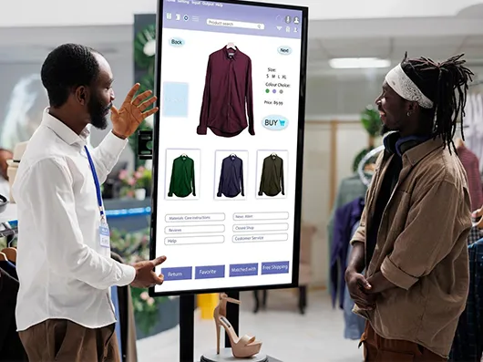 A store assistant showing a customer a shirt on a freestanding touchscreen